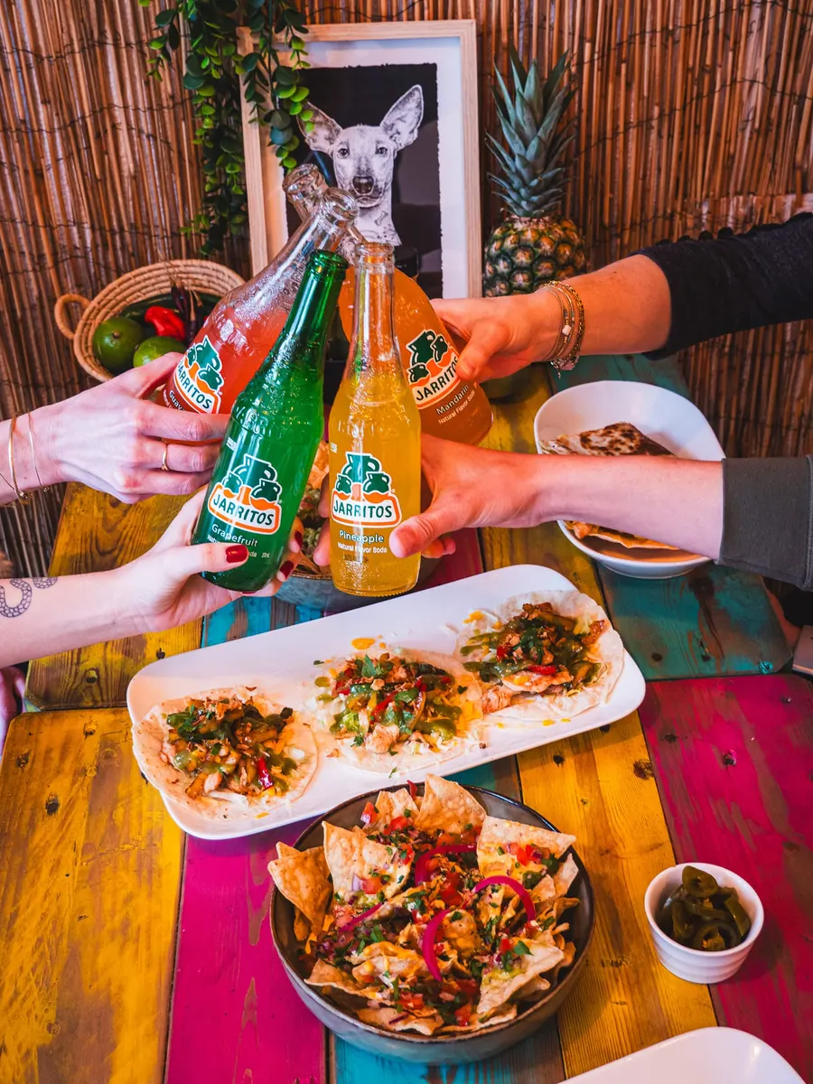 Des clients trinquent avec des sodas Jarritos autour de tacos et de nachos