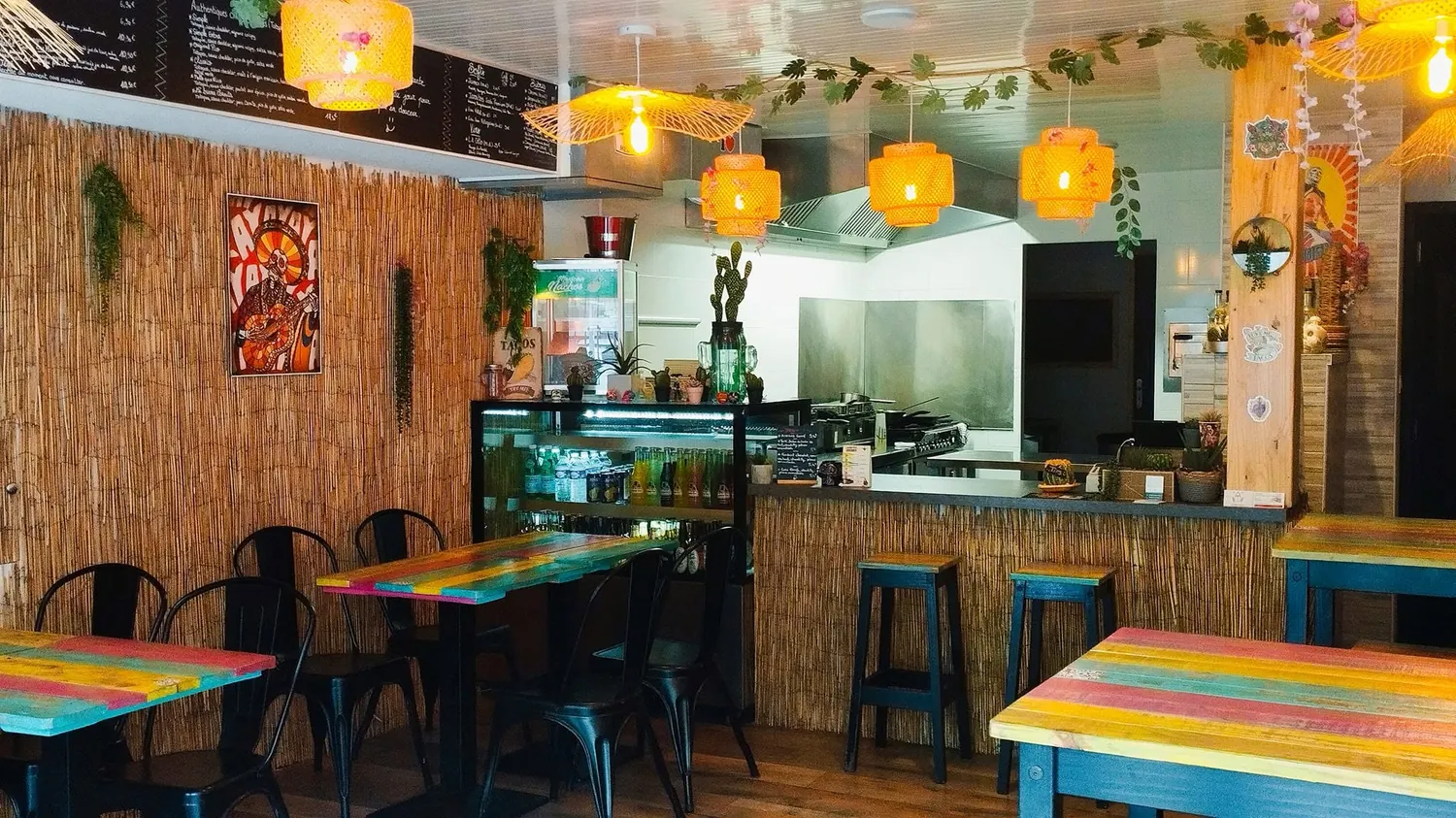 La salle du restaurant : tables colorées, murs en bambou, cuisine ouverte